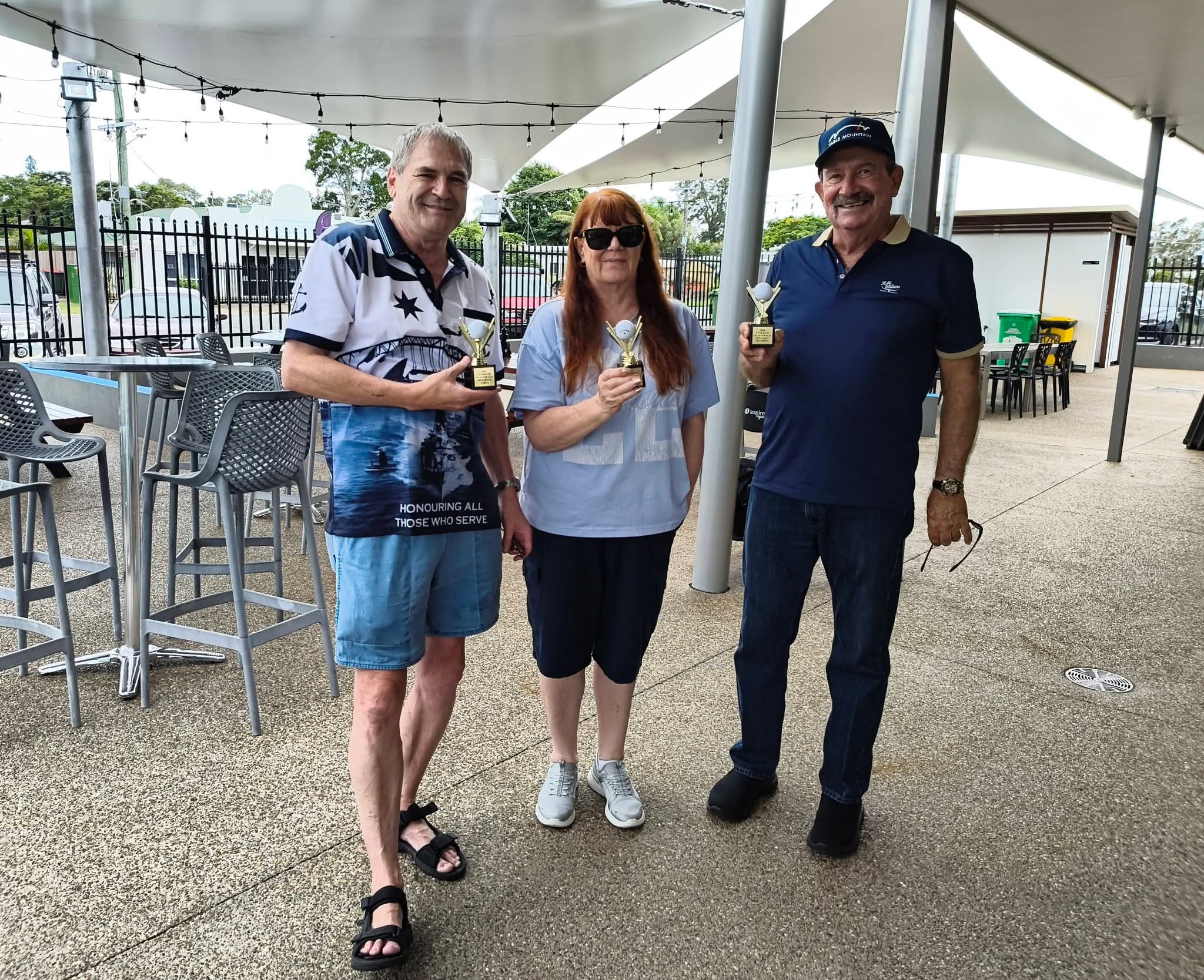 Three people holding trophies outdoors