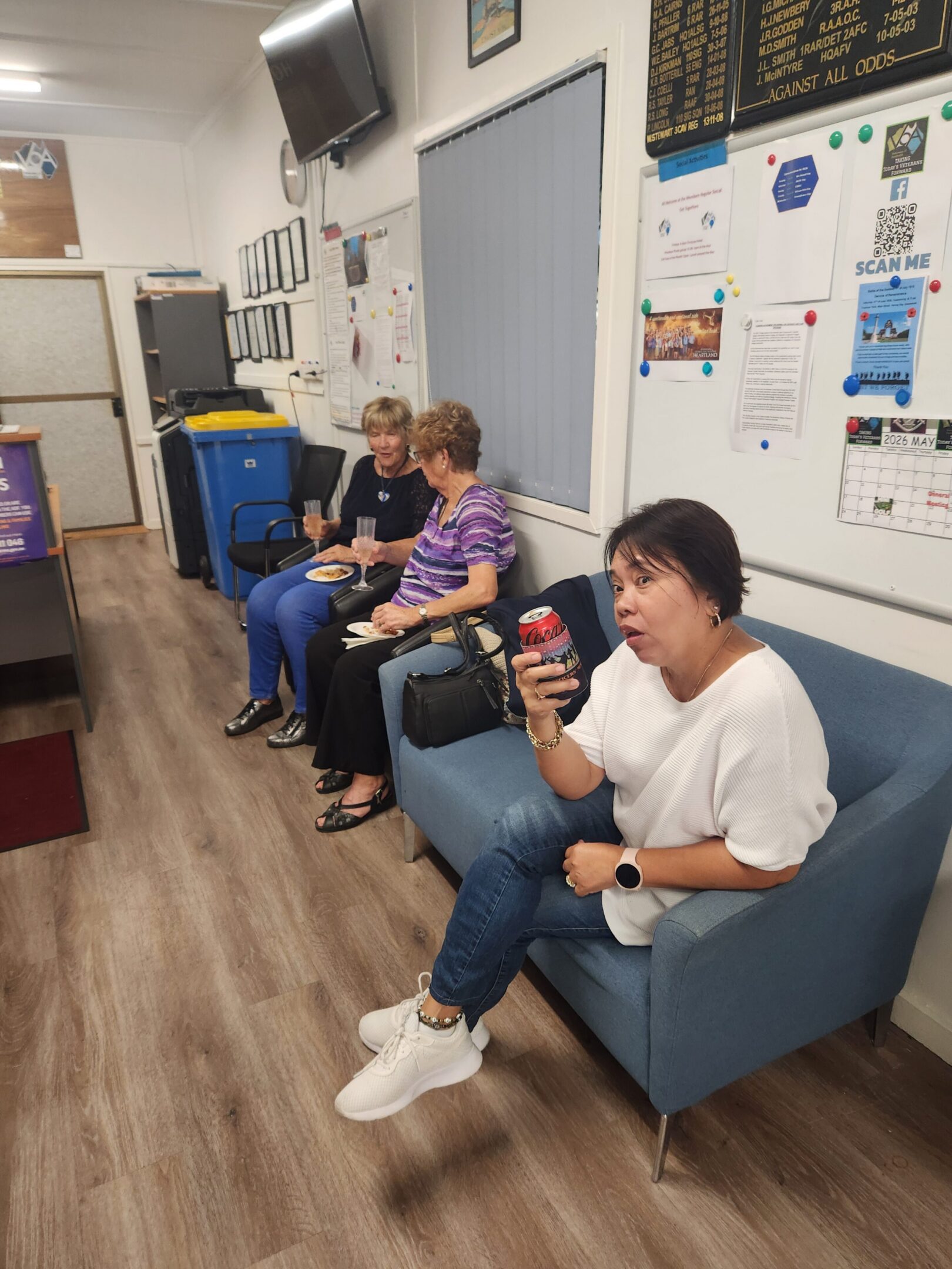 Three women seated in waiting room, one drinking