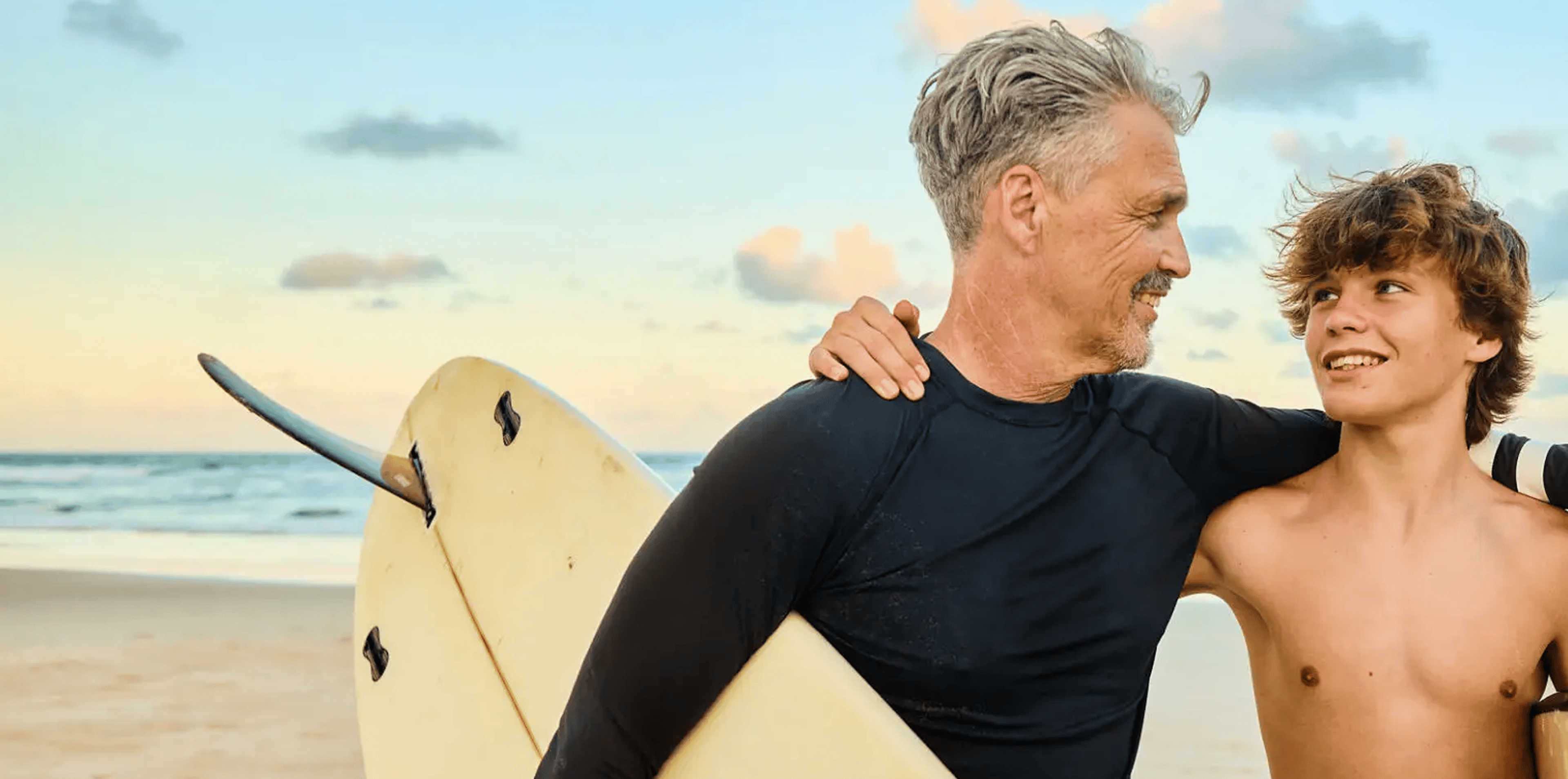 Man and teenage boy with surfboard on beach