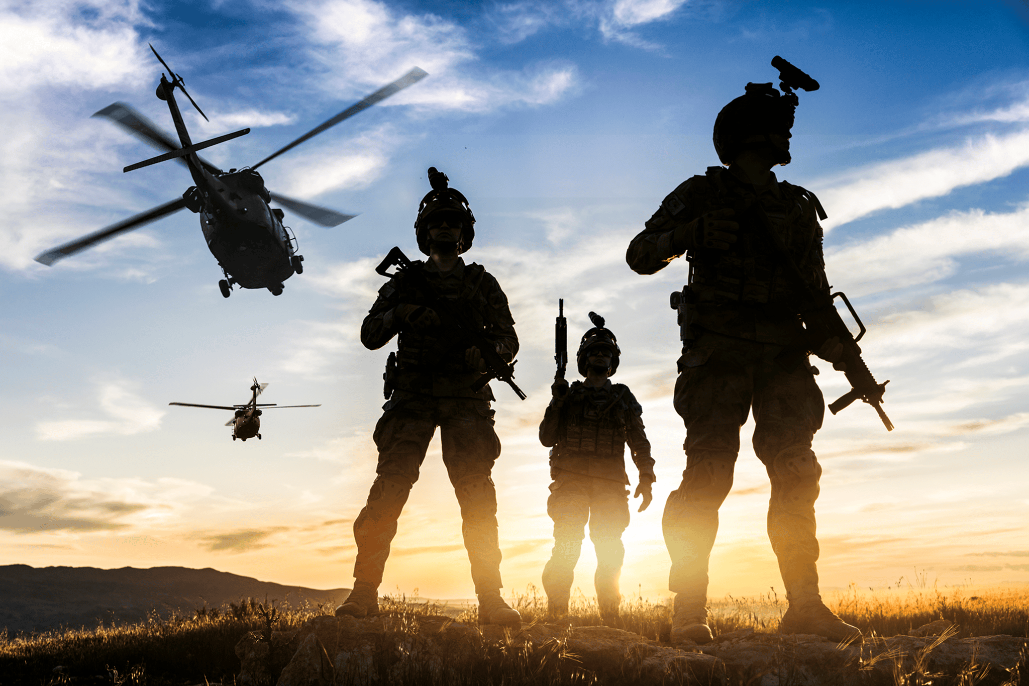 Silhouetted soldiers at sunset with helicopters